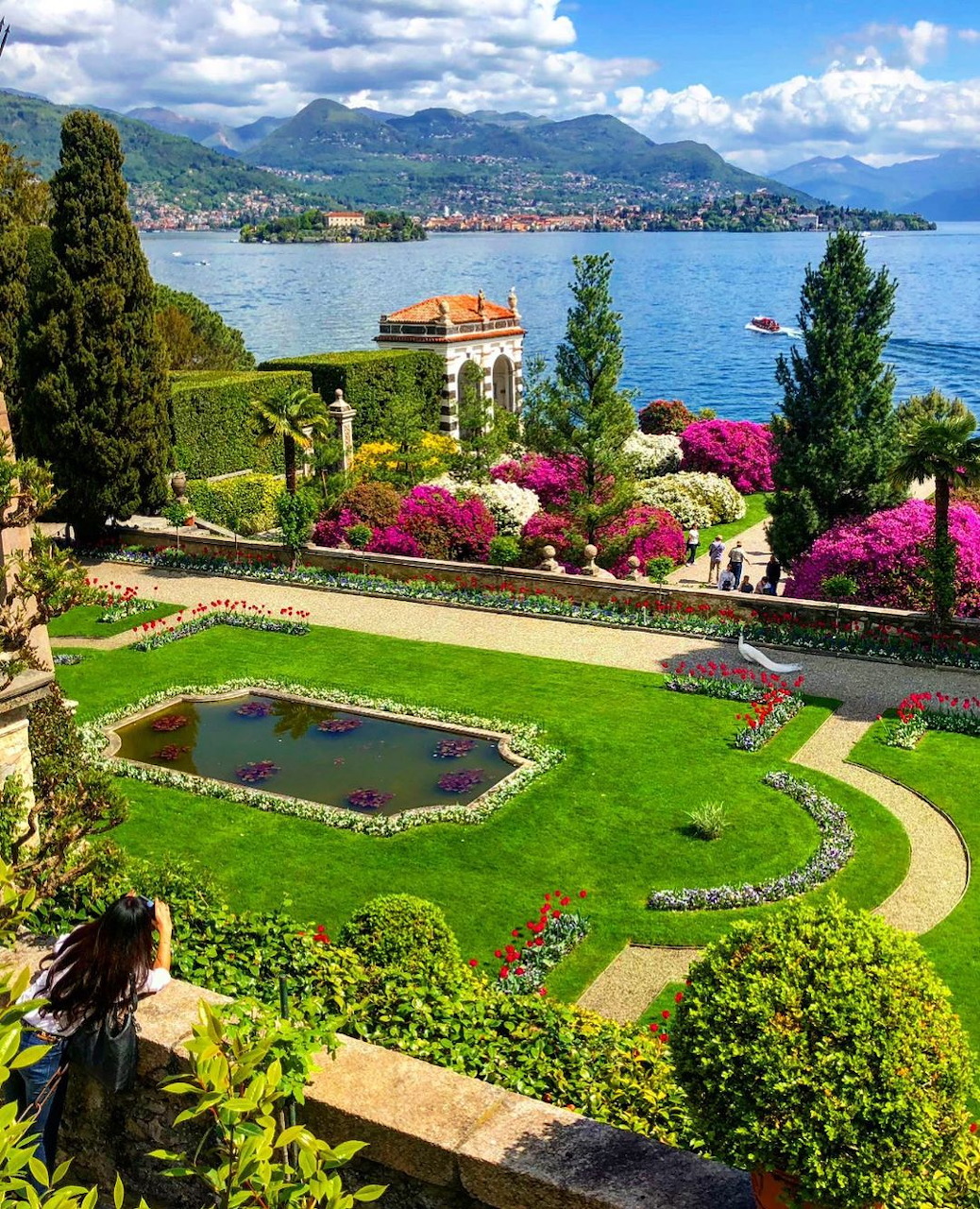 Formal Italian villa garden with flowering shrubs and pond overlooking a scenic mountain lake