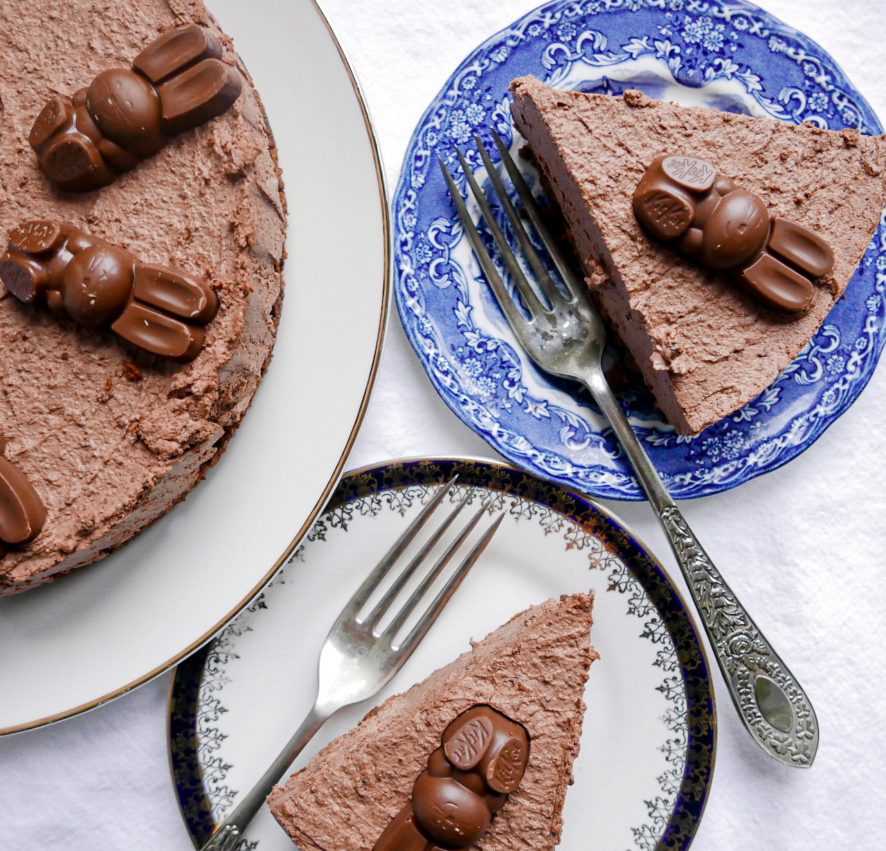 Whole chocolate cheesecake and two slices on decorative plates with forks, topped with chocolate bunny candies