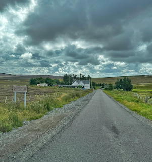 White inn building at end of empty country road under stormy clouds in Scottish Highlands