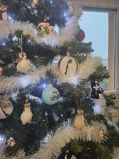 White Christmas tree decorated with assorted ornaments including figurines and glass baubles near a window