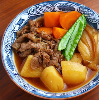 Bowl of nikujaga with beef, potatoes, carrots and snap peas in broth
