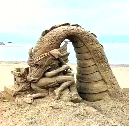 Sand sculpture of a dragon on a beach near the ocean