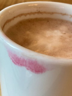 Close-up of a white coffee cup with foam and a pink lipstick mark on the rim