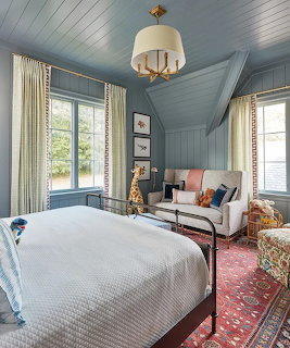 Cozy bedroom with blue-gray wood paneling, white bed, sitting area, and decorative rug