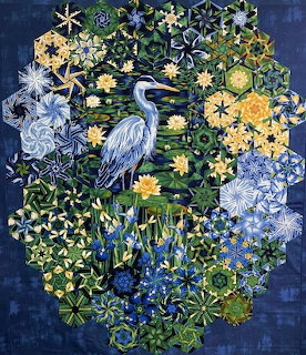 Patchwork quilt depicting a blue heron amid hexagonal floral and star patterns in blue, green, and yellow
