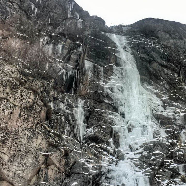 Partly frozen waterfall cascading down a steep dark rock face in winter