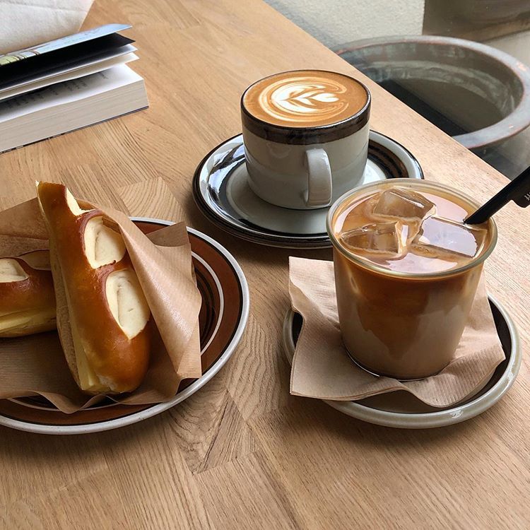 Two coffee drinks with latte art, croissant pastries, and a book on a wooden table