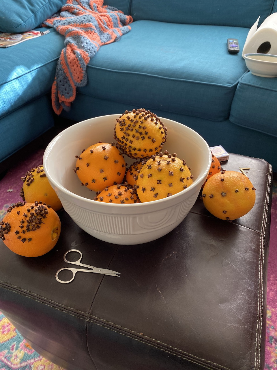 Bowl of clove-studded oranges on a dark ottoman beside a blue sofa