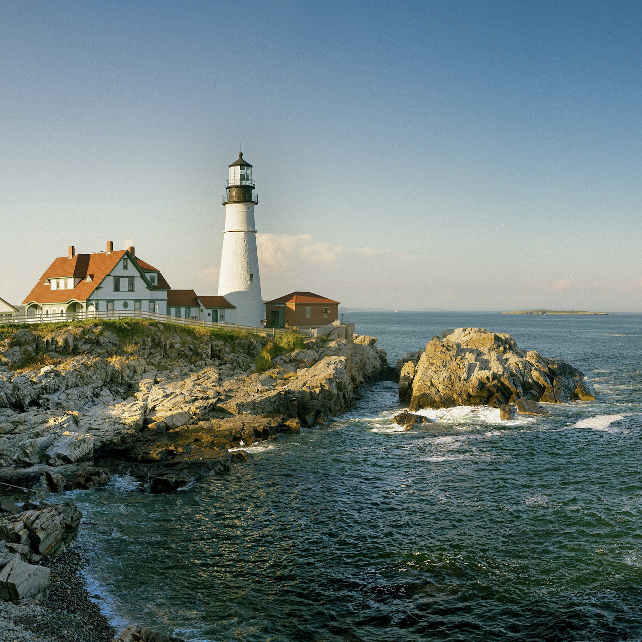 White lighthouse and house on rocky coast beside the ocean