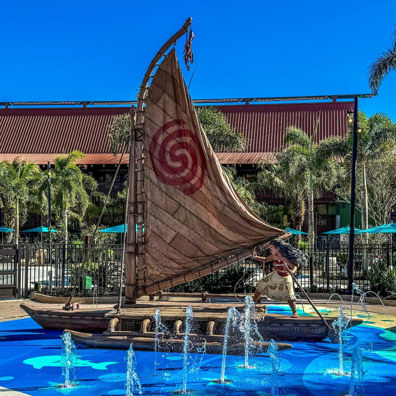 Polynesian boat sculpture with red spiral sail in fountain plaza with palm trees