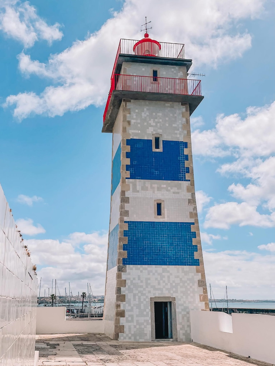 Blue and white lighthouse tower in Cascais beneath a bright cloudy sky