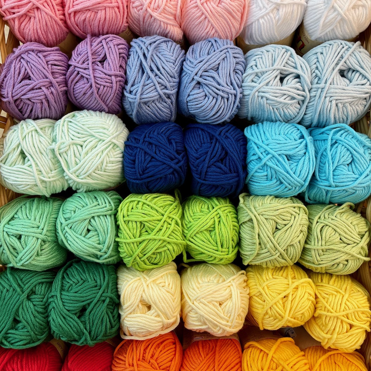 Neatly organized rows of colorful yarn balls arranged in rainbow gradient from pink to orange on display shelves