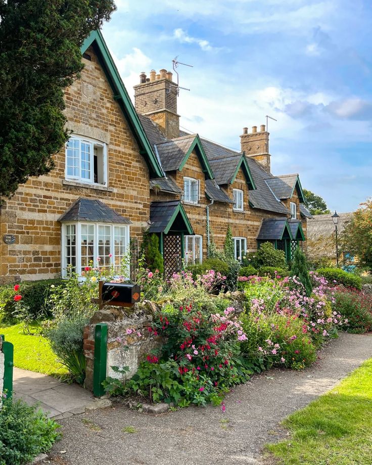 Stone Cotswold cottages with flowers and a garden path under a blue sky