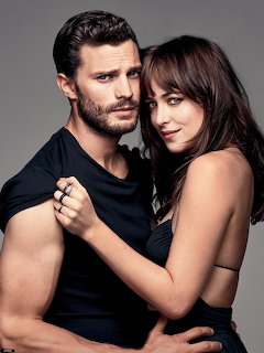 Man and woman posing together in a dark studio portrait, she embraces him from behind