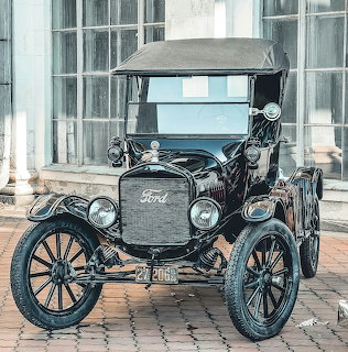 Front view of a black vintage Ford car parked in front of tall windows