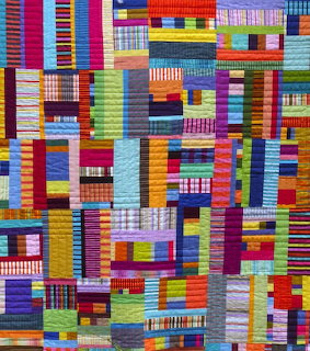 Colorful patchwork quilt with geometric fabric strips in red, blue, yellow, green, and purple arranged in abstract pattern