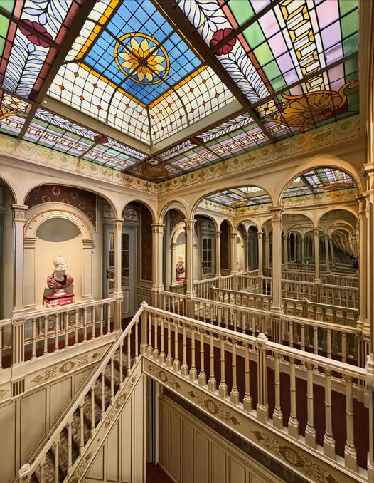Art Nouveau building interior with ornate stained glass skylight and multi-level galleries with arched windows