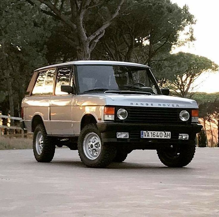 Classic Range Rover SUV parked on a road with trees behind it