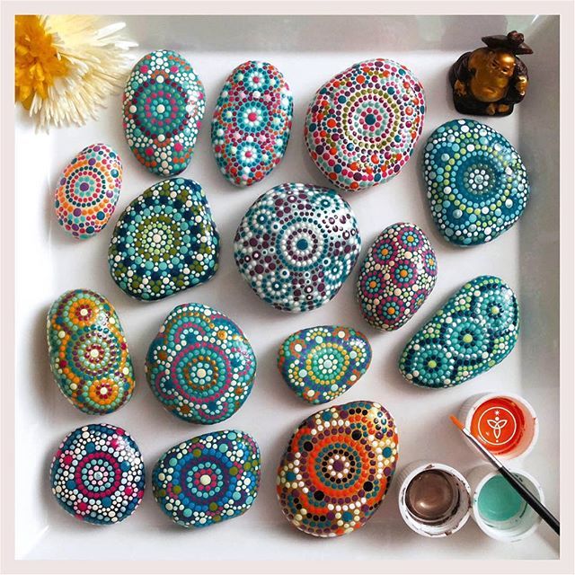 Hand-painted stones with intricate mandala dot patterns in various colors arranged on white background