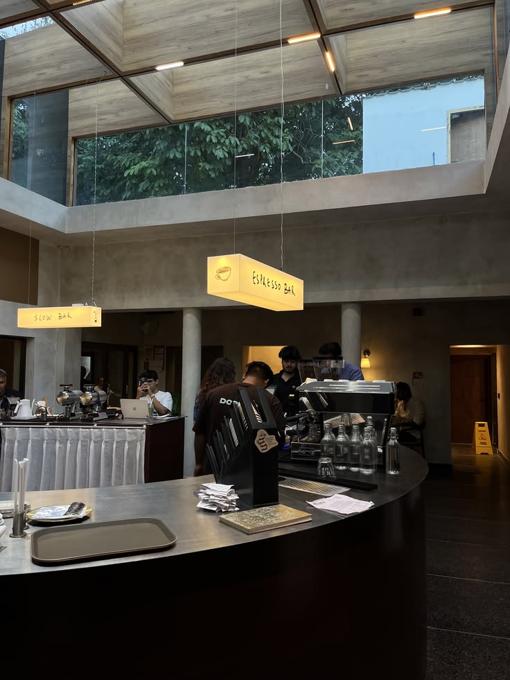 Modern espresso bar interior with concrete walls, skylights, yellow signage, and baristas behind the counter