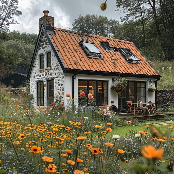 White cottage with orange roof nestled in garden of orange flowers and green forest