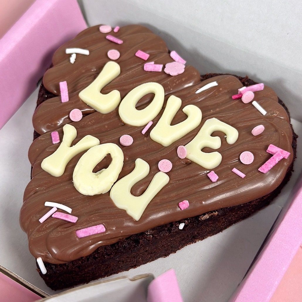 Heart-shaped chocolate cake decorated with Love You text and pink sprinkles in white gift box