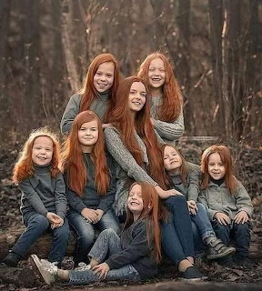 Mother and six red-haired girls posing together in a forest clearing