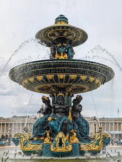 Ornate bronze fountain with gold accents and multiple tiers in Paris plaza with water streams and cloudy sky background