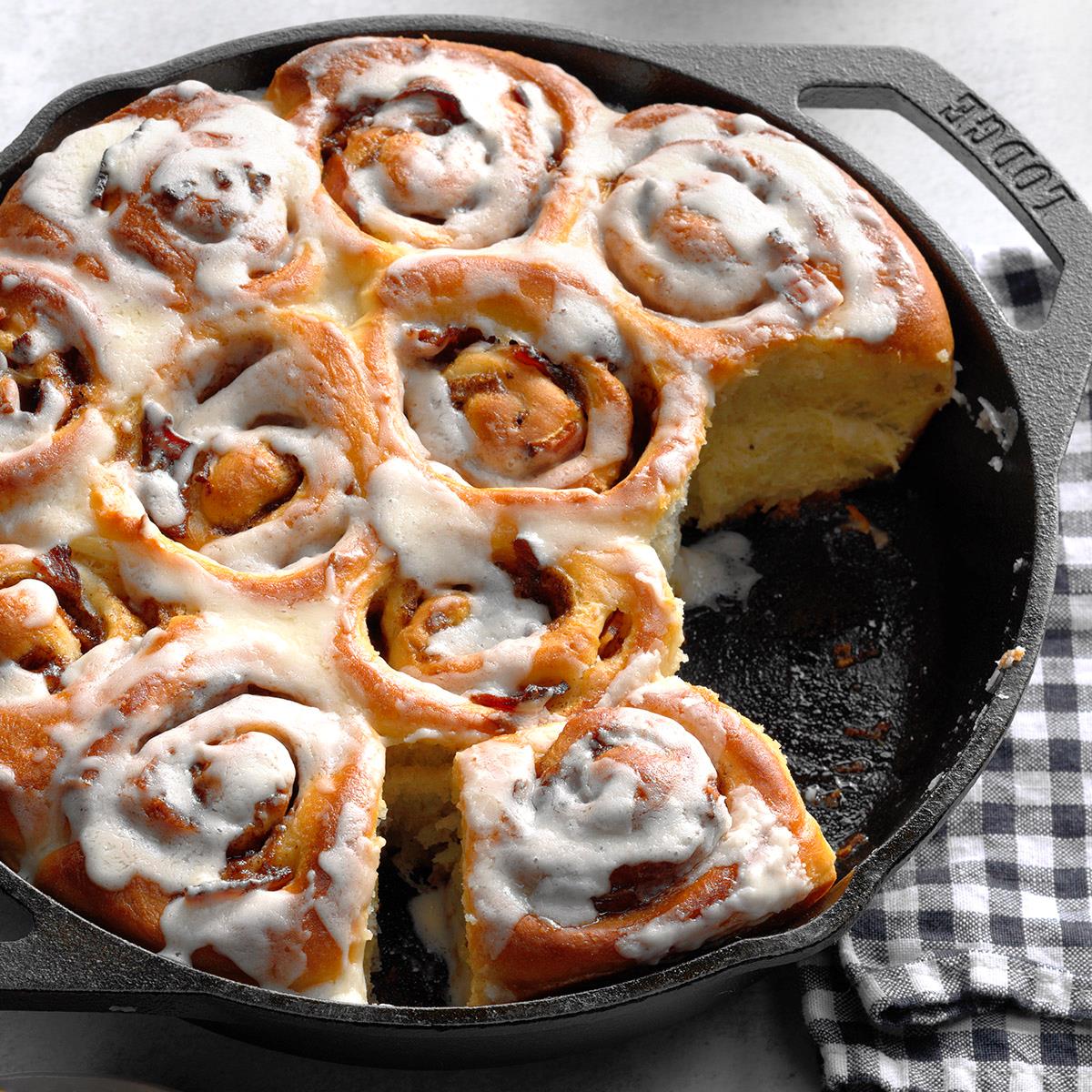 Frosted cinnamon rolls with bacon in a cast iron skillet on checkered cloth