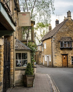 Narrow street in a Cotswold village with golden stone buildings and a perfumery shop sign