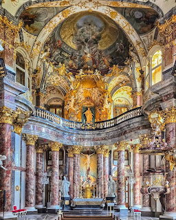 Ornate baroque church interior with gold details, frescoed dome, marble columns, and elaborate altar