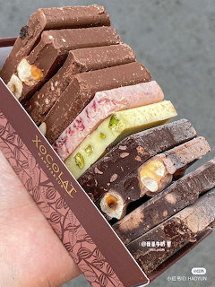 Hand holding an open box of assorted chocolate bars with various filings and flavors