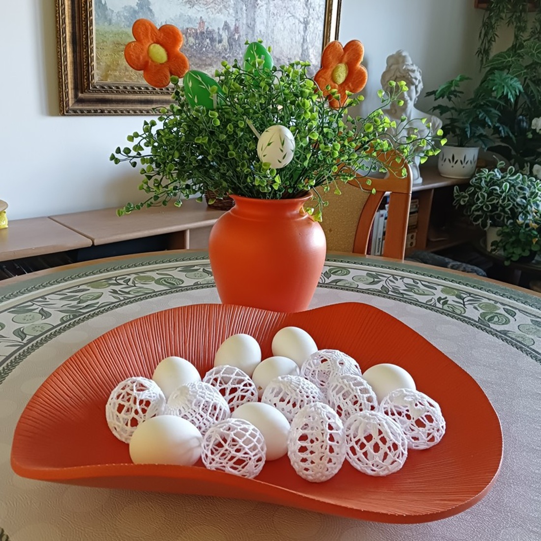 White crocheted Easter eggs on orange tray with flower arrangement