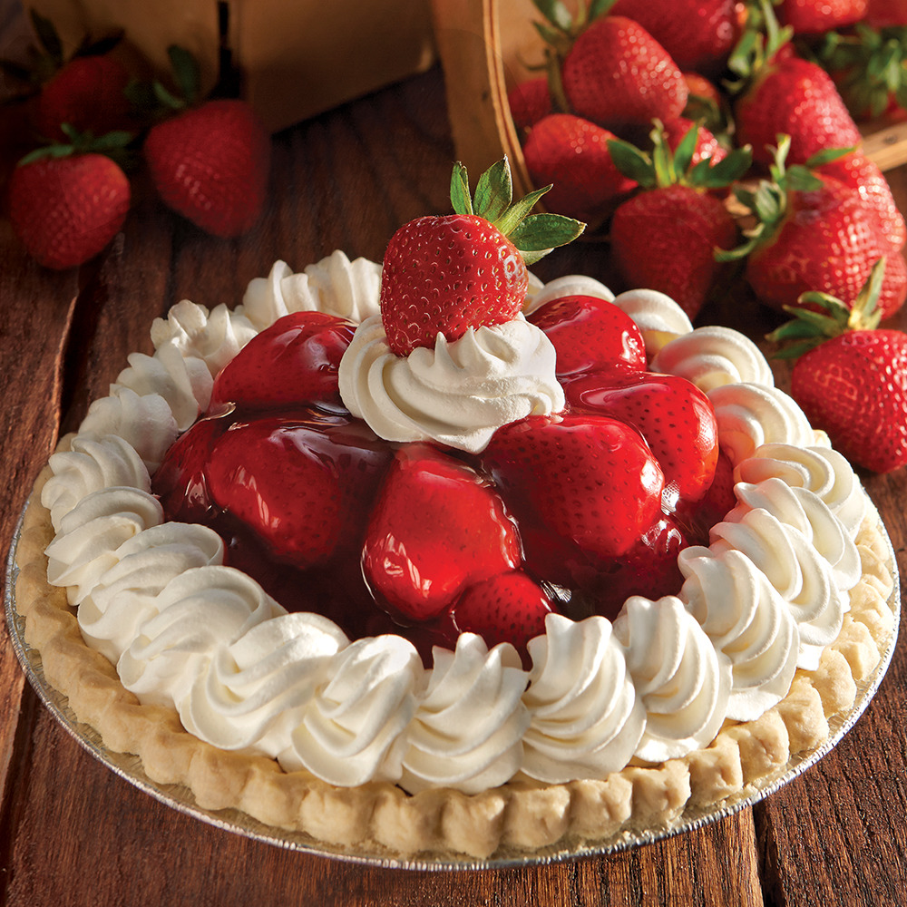 Strawberry pie topped with glazed berries and whipped cream on wooden surface with fresh strawberries