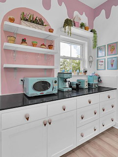 Bright kitchen with white cabinets, turquoise retro appliances, pink shelves, and decorative pink drip molding on walls