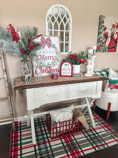 Christmas console table with white arch mirror, red and green decorations, plaid rug, and festive holiday accents
