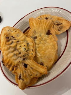 Two golden taiyaki fish-shaped pastries with red bean filling on a white and red ceramic plate