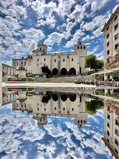 White historic building with twin towers reflected in calm water beneath blue sky with puffy clouds