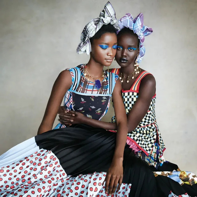 Two fashion models in patterned dresses and headwraps posing together in a studio portrait