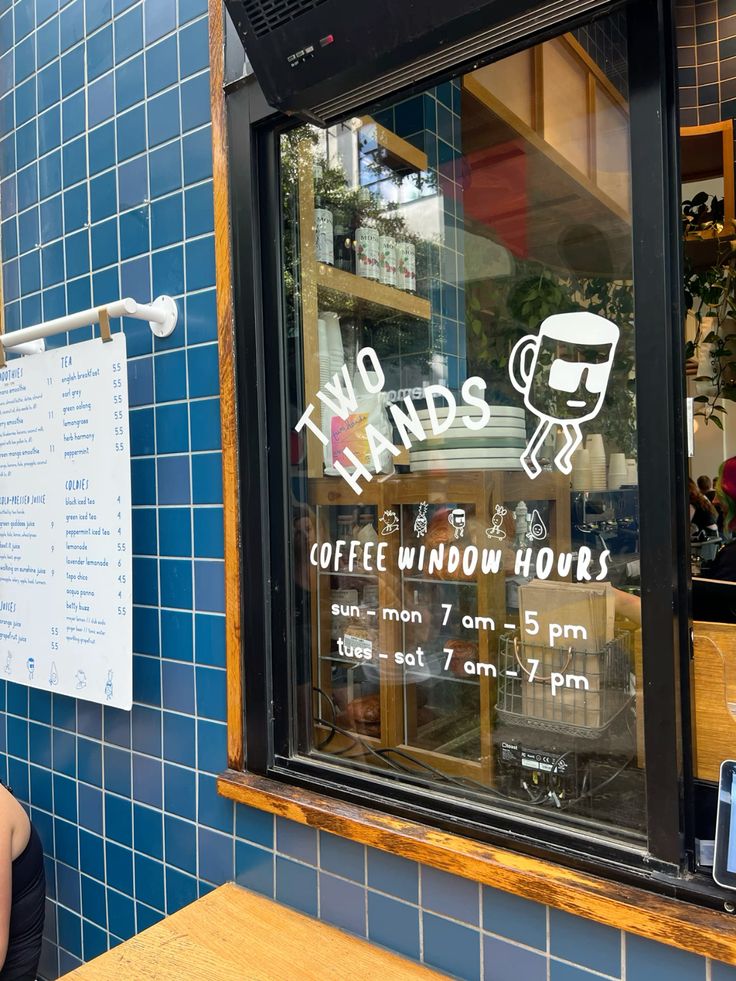 Two Hands coffee window with painted hours sign on glass, surrounded by blue tiles