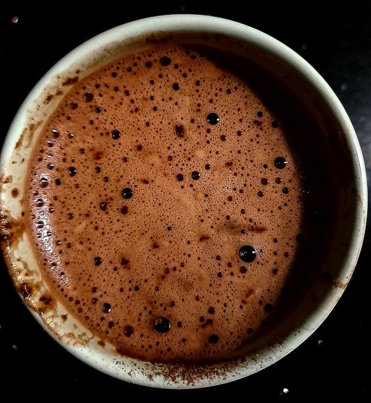 Top view of a cup of dark coffee with bubbly foam on a black background