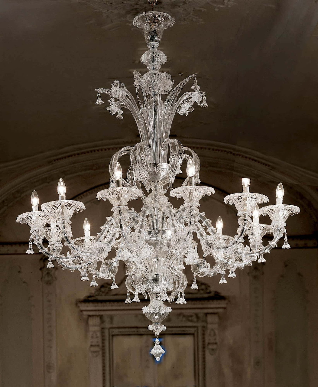 Ornate clear Murano glass chandelier hanging indoors beneath a dark arched ceiling