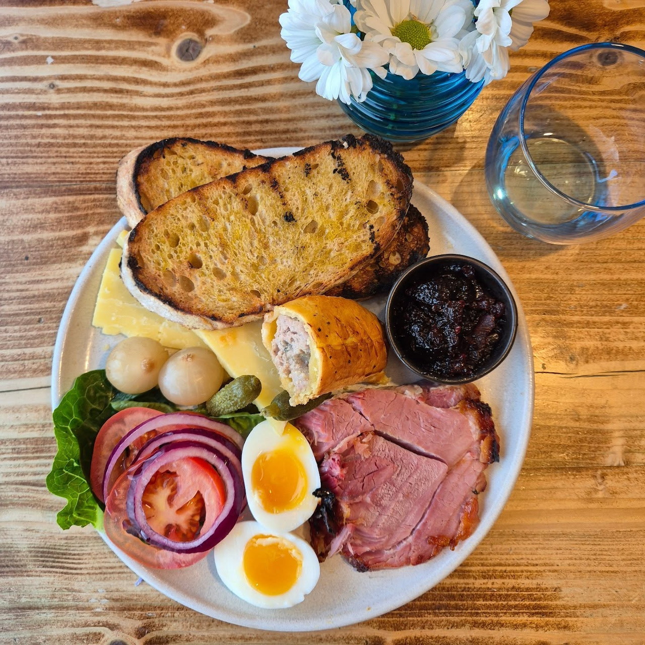 Overhead view of a ploughman's lunch platter with bread, cheese, cold meats, eggs, and pickles on a white plate