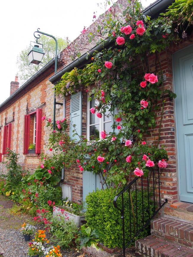 Brick cottage facade covered with climbing roses and colorful flowers in Gerberoy, France