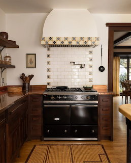 Rustic kitchen with black vintage stove, white tile backsplash, wood cabinets, and large white hood