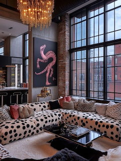 Modern loft living room with spotted sofas, brick wall, large windows, gold chandelier, and octopus painting
