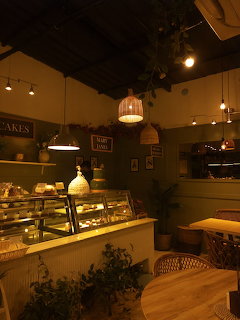 Warmly lit café interior with cake display counter, wicker hanging lamps, and plants