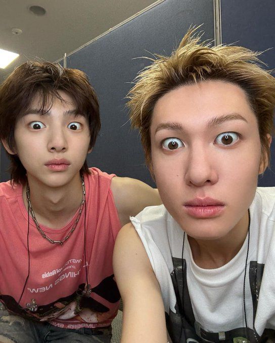 Two young men making exaggerated wide-eyed expressions in a selfie, one in pink shirt, one in white