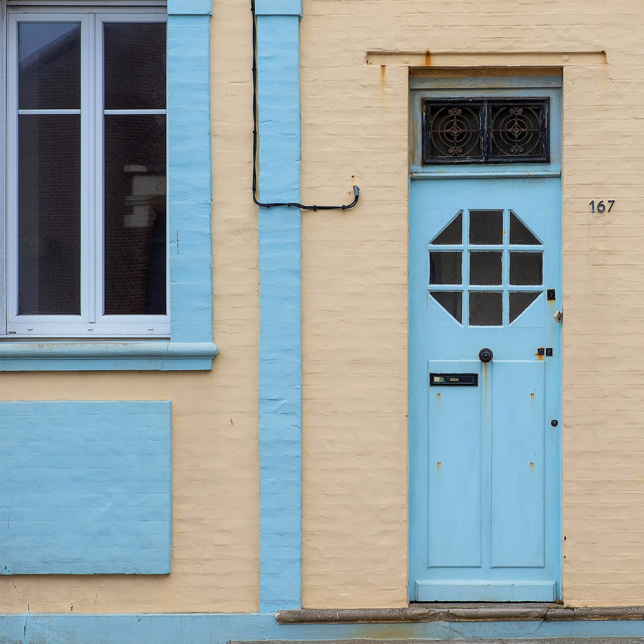 Light blue door with ornate window on yellow building wall, number 167 visible