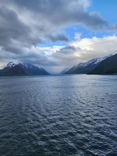 Norwegian fjord with snow-capped mountains and cloudy sky reflected in calm blue water